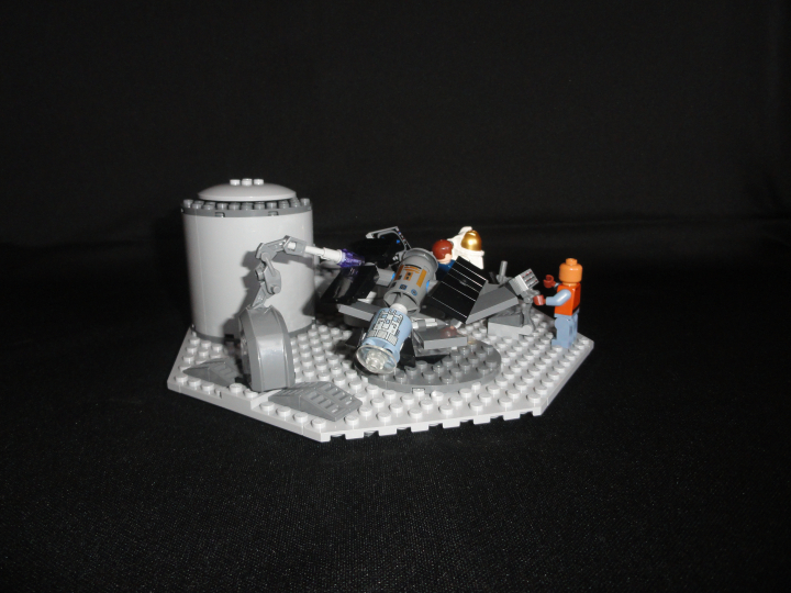 LEGO MOC - Потому что мы можем! - Вперёд, к звездам!: Как я говорил выше, раз уж мы готовы потратить огромный деньги на этот полёт, почему бы не сделать что нибудь полезное, например, вывести на земную орбиту спутник, который позволит точнее предсказывать погоды, составлять карту в реальном времени, доставлять кабельное в ваши дома или просто следить за всеми вами?<br />
Удобная вещь, не правда ли?<br />
Инженер, скромно стоящий за пультом управления дорабатывает систему, позволяющую  позволяющую спутнику накапливать космическую энергию, чтобы обеспечить бесперебойное функционирование всех систем (спустя много лет эти наработки приведут к созданию гибких солнечных батарей), но пока это лишь идея.<br />
